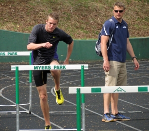 As Queens track coach Jim Vahrenkamp, right, looks on, Queens men's track athlete Johannes Reimann, left, works on his hurdling technique during a recent practice at Myers Park High School. CREDIT: Bill Kiser